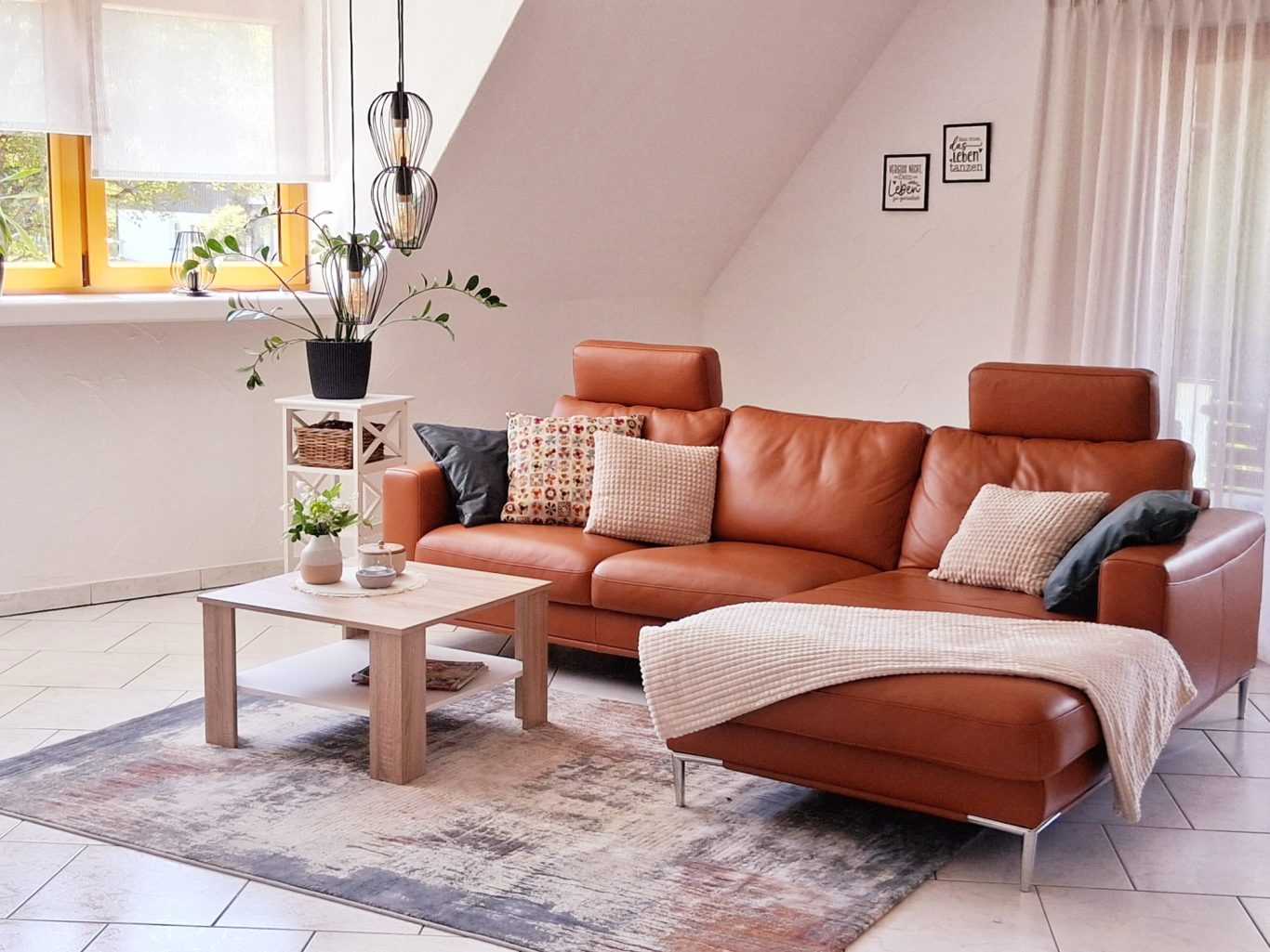 Wohnzimmer Heller Wohnbereich mit braunem Ledersofa, Tisch und dekorativen Kissen.